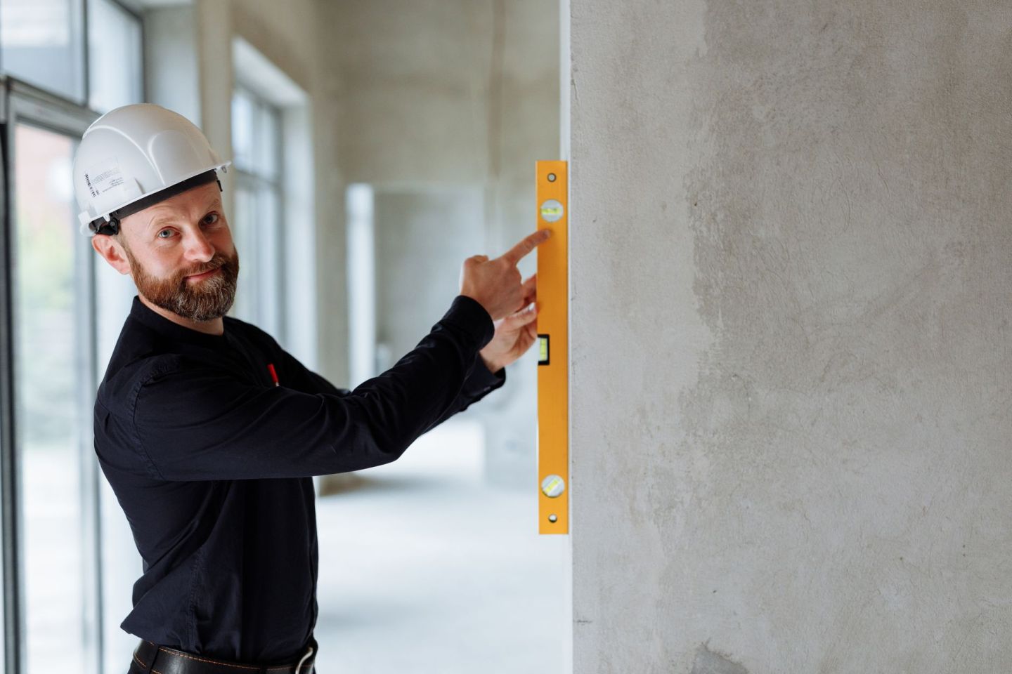 Fachmann mit Schutzhelm prüft eine Betonwand mit einer Wasserwaage